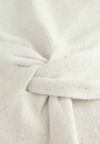 Close-up of soft beige fabric with a knot detail, featuring small shiny sequins scattered across the textured surface.