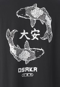 Černé tričko s bílým grafickým designem dvou kaprů koi a japonských znaků. Pod designem ryb je text "OSAKA".