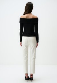 Zwarte off-the-shoulder top met lange mouwen, gecombineerd met witte rechte pijpen en zwarte hoge hakken, wat zorgt voor een strakke silhouette.