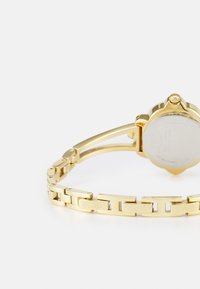 Gold-toned wristwatch with a linked bracelet and round case. Features a smooth surface, glass face, and engraved brand detail on band.