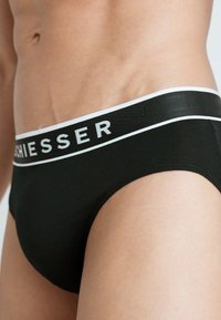 Schwarze Baumwollslips mit einem weißen Gummibund, der den Markennamen "Schliesser" zeigt. Enganliegendes Design mit glatter Textur.