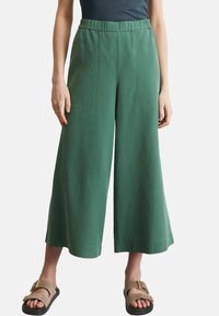 Pantaloni verdi a gamba larga con vita elastica, realizzati in tessuto leggero. Presentano tasche laterali e una texture liscia e opaca.