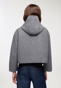 Felpa grigia in lana accorciata con un ampio cappuccio. Presenta spalle scese e una consistenza morbida. Abbinata a jeans in denim blu scuro.