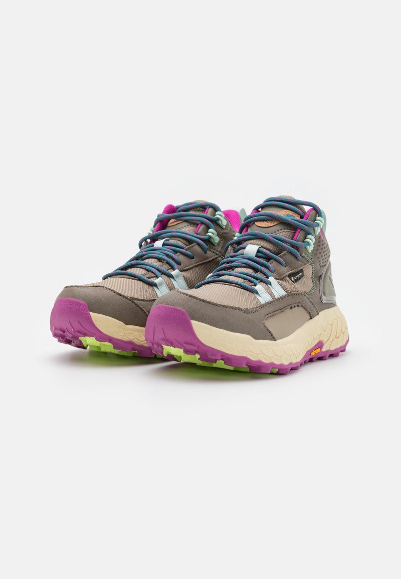 Zapatos de senderismo grises con parte superior de tela texturizada, cordones multicolores, una entresuela color crema y una suela de goma rosa y verde.