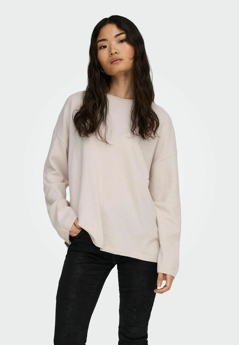 Sudadera de manga larga beige claro con un ajuste relajado y cuello redondeado, combinada con pantalones negros texturizados. Diseño sencillo, tejido suave.