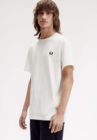 Weißes Baumwoll-T-Shirt mit kurzen Ärmeln und rundem Ausschnitt. Mit einem kleinen schwarzen Logo auf der linken Brust. Lockerer Schnitt.