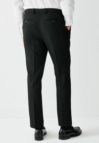 Mustad kohandatud püksid sirgjoonelise säärega, millel on kaks selja taskut nuppudega ja sile tekstuur. Sobitatud mustade kingadega.