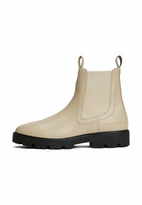 Botín Chelsea de cuero beige con paneles laterales elásticos, lengüetas para facilitar el calzado y suela de goma negra resistente. Detalle sutil del logo en el lado exterior.