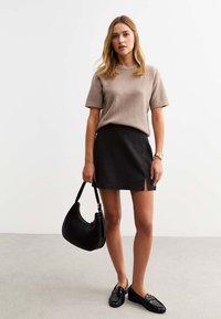 Top de punto beige de manga corta combinado con una minifalda de cuero negra con una abertura lateral. Lleva un bolso negro y usa mocasines negros.