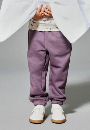 Child wearing purple sweatpants and white sneakers, hands clasped, with a white blanket draped over the upper body.