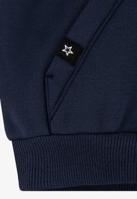 Navy blue sweatshirt featuring a textured knit, ribbed cuffs and hem, with a black label displaying a white star logo on the side.