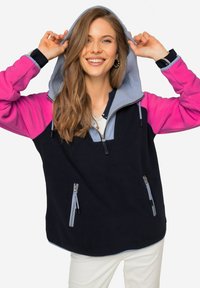 Pullover in pile con corpo blu navy, maniche rosa e cappuccio azzurro chiaro. Presenta tasche con zip e colletto a mezza zip. Tessuto testurizzato.