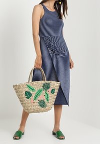 Navy sukienka w paski z marszczonym boku, zestawiona z dużą plecioną torbą ze słomy, ozdobioną haftem w zielone i różowe liście. Zielone buty wsuwane.