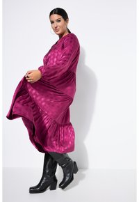 Fuchsia Satin-Kleid mit einem strukturierten Punktenmuster, langen Ärmeln und gestuftem Saum, kombiniert mit eleganten schwarzen kniehohen Stiefeln.