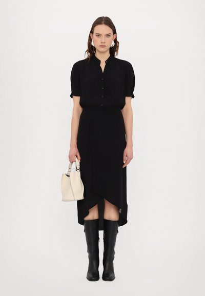 Rochie midi neagră cu guler butonat, mâneci scurte tip puff, tiv asimetric, asortată cu cizme negre până la genunchi și o poșetă mică albă.