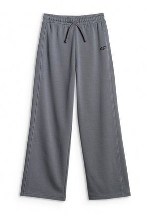 Młoda dziewczyna w szarej czapce, oversize koszulce w ciemnozielony i szary ombre, luźnych szarych spodniach, białych sneakersach, niosąca zieloną torbę na ramię.