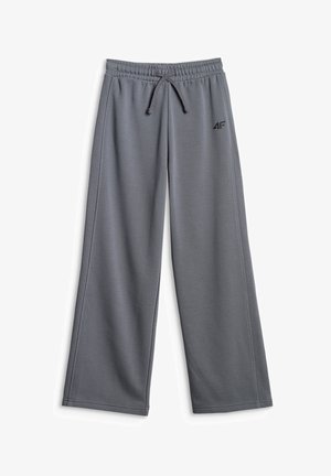 Jeune fille portant un bonnet gris, un t-shirt oversize ombré vert foncé et gris, un pantalon gris ample, des baskets blanches, portant un sac à bandoulière vert.