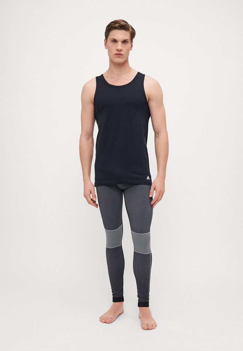Dunkelblaues ärmelloses Tanktop kombiniert mit enganliegenden grauen Leggings, die über Mesh-Details und subtile reflektierende Akzente an den Seiten verfügen.