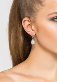 Silver teardrop earrings with a textured surface, featuring a small hoop attachment. The design is shiny and reflective, enhancing visual appeal.