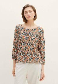 Blumenbluse mit langen Ärmeln, die eine Mischung aus orangefarbenen, türkisfarbenen und weißen Mustern aufweist, aus leichtem Stoff mit einem runden Ausschnitt gefertigt.