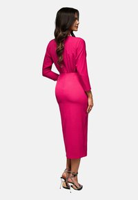 Vaaleanpunainen, muotoon ommeltu mekko, jossa on pitkät hihat, polvipituinen malli ja tiukka vyötärö. Yhdistettynä kärkikorkoisilla sandaaleilla.