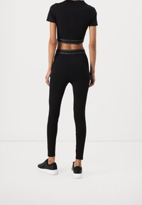 Top court noir et leggings taille haute, design ajusté, texture lisse, bord blanc contrastant, associés à des baskets noires.