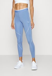 Niebieskie legginsy sportowe z białymi akcentowanymi szwami, wysokim stanem i dopasowanym krojem. Dobrane z białymi butami sportowymi.