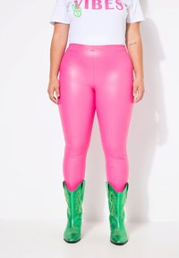 Leggings rosa lucidi abbinati a stivali da cowboy verdi con motivi testurizzati. La parte superiore è una camicia bianca con testi colorati.