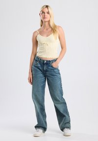 Light yellow ribbed crop top with scalloped edges and tie detail, paired with loose-fitting blue denim jeans and white sneakers.