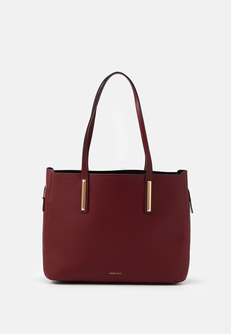 Burgundská kožená taška přes rameno s dvojitými popruhy, zlatými obdélníkovými akcenty a malým logem značky umístěným ve spodní části.