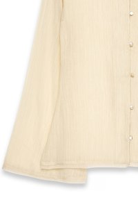 Blusa button-up di colore crema con maniche lunghe, tessuto testurizzato e cinque bottoni rotondi lungo la parte frontale. L'orlo è leggermente curvo.