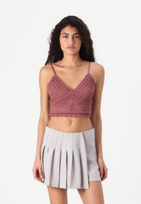 Heklet crop top i støvet rosa med V-hals og bølgekant, kombinert med et grått, plissert A-linje mini skjørt. Glatte teksturer gjennomgående.