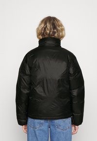 Sort puffjakke med høj krave, glat tekstur og sidelommer. Båret over lyseblå denimjeans.