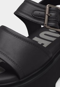 Μαύρο δερμάτινο σανδάλι πλατφόρμα με φαρδιές λουρίδες και μεταλλική αγκράφα στο λουράκι του αστραγάλου.