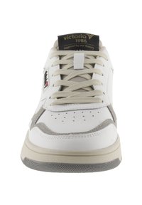Sneaker bianco con tomaia in pelle liscia, dettagli in suede grigio, punta perforata e suola in gomma crema. Presenta lacci beige e branding sulla linguetta.