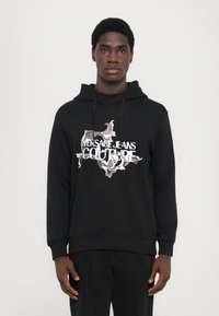 Sweatshirt preto com capuz, apresentando uma gráfica frontal com designs ornamentais e um logotipo em texto branco destacado, feito de um tecido suave com punhos canelados.