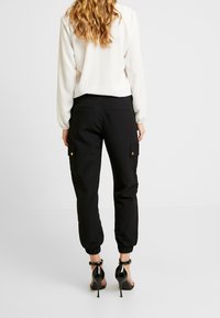 Celana kargo hitam dengan manset elastis, dilengkapi dengan saku samping dan bahan yang halus. Dipadukan dengan atasan putih lengan panjang dan sepatu hak hitam.