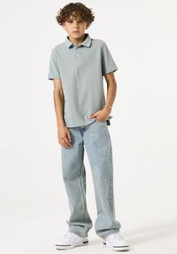 Polo vert clair, à manches courtes, avec un col. Associé à un jean ample bleu clair et des baskets blanches. Design simple avec des détails minimaux.