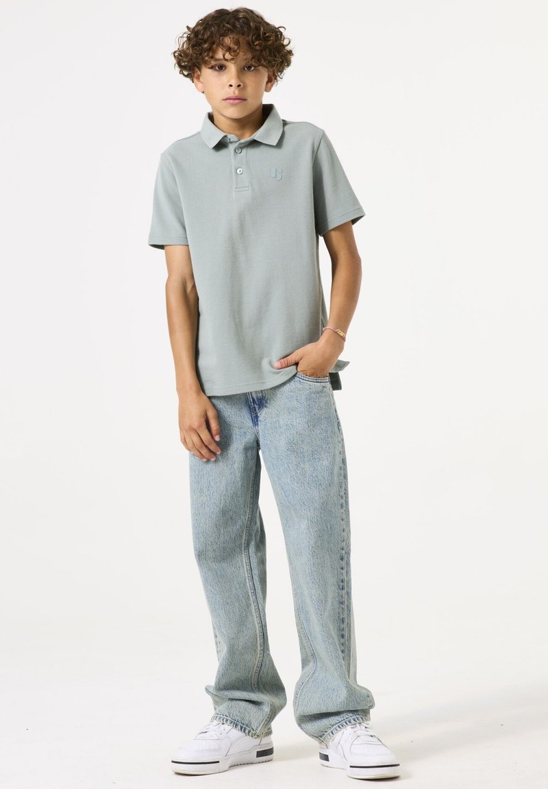 Polo vert clair, à manches courtes, avec un col. Associé à un jean ample bleu clair et des baskets blanches. Design simple avec des détails minimaux.