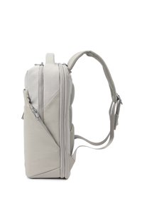 Sac à dos gris clair avec plusieurs compartiments zippés et une sangle d’épaule rembourrée et réglable, vu de côté.