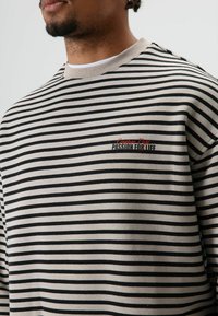 Gestreepte trui in crème en zwart, met een ronde hals en geborduurde tekst "Creative Dept. Passion for Life" op de borst.