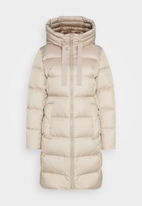 Abrigo acolchado color beige con cuello alto, cierre de cremallera y dos bolsillos delanteros. La tela presenta una textura suave con un patrón acolchado horizontal.