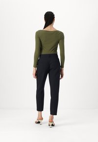 Haut à manches longues, vert olive associé à un pantalon taillé, bleu marine foncé. Fond blanc, tissu uni, et design simple sans motifs.