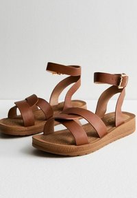 Sandales en cuir marron avec plusieurs brides entrecroisées, boucle à la cheville et semelle rembourrée. Le design présente une semelle intérieure texturée pour le confort.