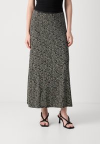 Jupe maxi en tissu noir avec un motif abstrait beige, dotée d'une taille ajustée et d'un design fluide. Associée à des sandales à talons noires à lanières.