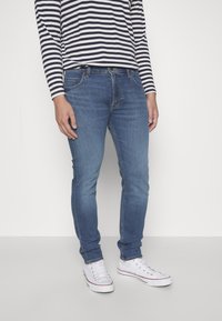 Dark blue skinny jeans with front pockets, worn with a navy and white striped long-sleeve shirt and white sneakers.