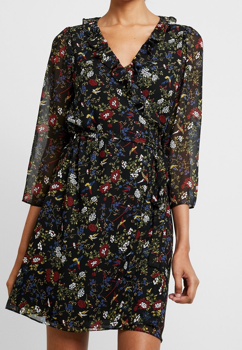 Vestido negro con flores, con un escote con volantes, mangas de tres cuartos y una cintura ajustable. Presenta patrones florales coloridos y una textura transparente.