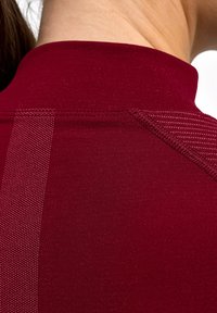 Top sportivo color marrone scuro con collo alto, dettaglio a righe strutturate e tessuto liscio. Cuciture visibili sulla spalla.