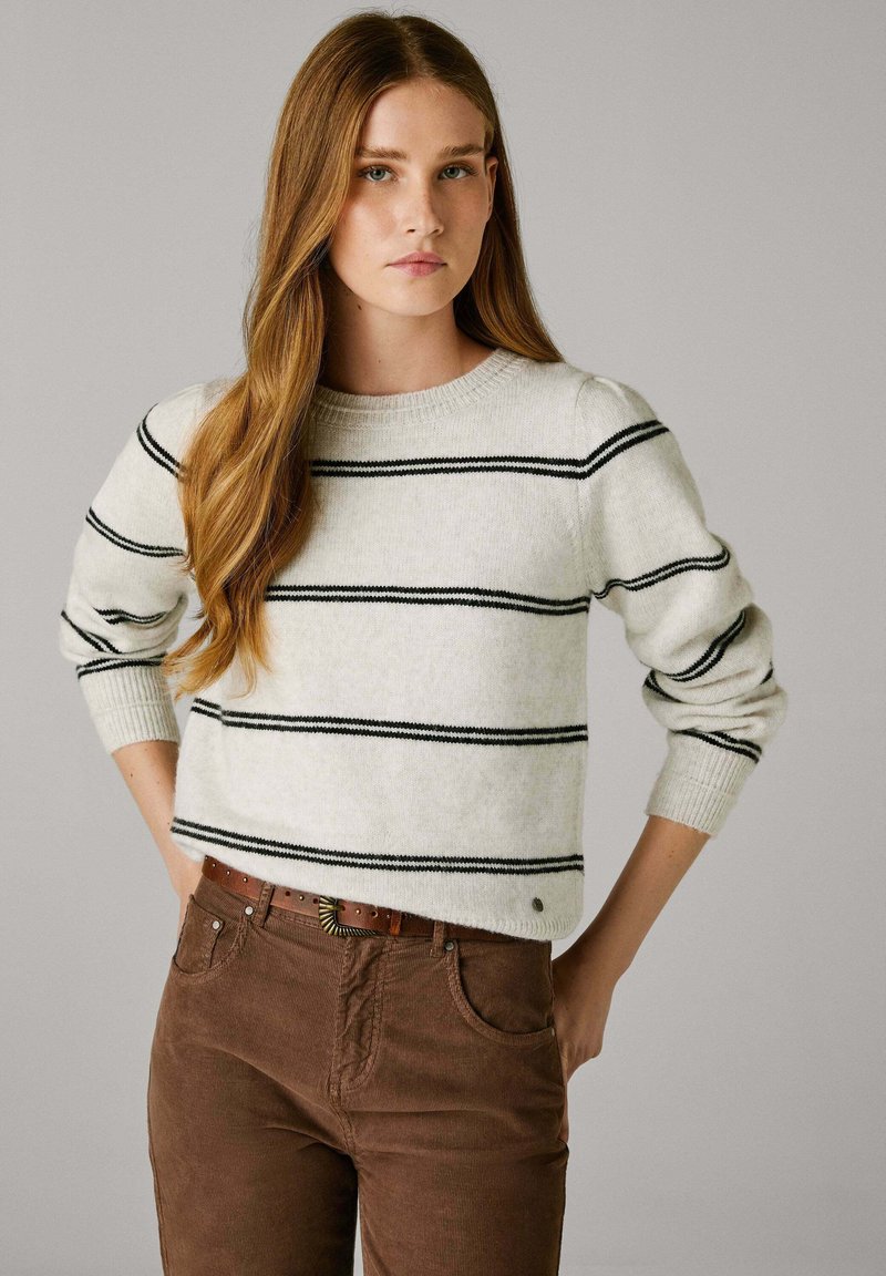 Svijetlosivi pulover s crnim horizontalnim prugama, okruglim izrezom i rebrastim manžetama, uparen s smeškim kordura hlačama i smeškim pojasom.