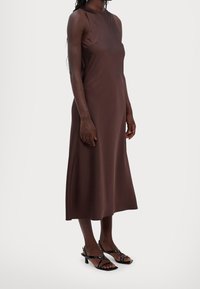 Braunes ärmelloses Midikleid mit hohem Ausschnitt, glatter Textur und A-Linie. Getragen mit schwarzen Riemchenheels.